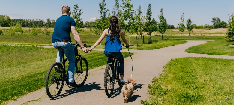 a couple rides their bikes with their dog in the emerald neckalce of Liberty Landing image